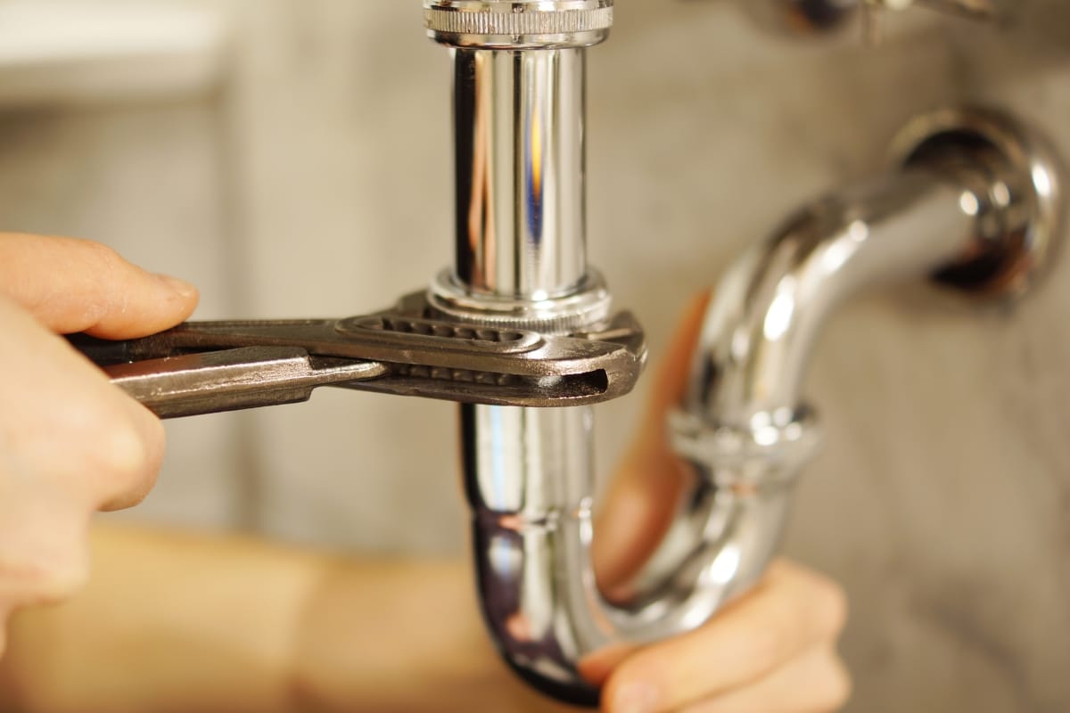 Plumbing and Septic Systems in Woodstock, GA: How They Work Together 8 A person uses a wrench to tighten a metal pipe beneath a sink, showing a close-up of plumbing and septic systems repair work.
