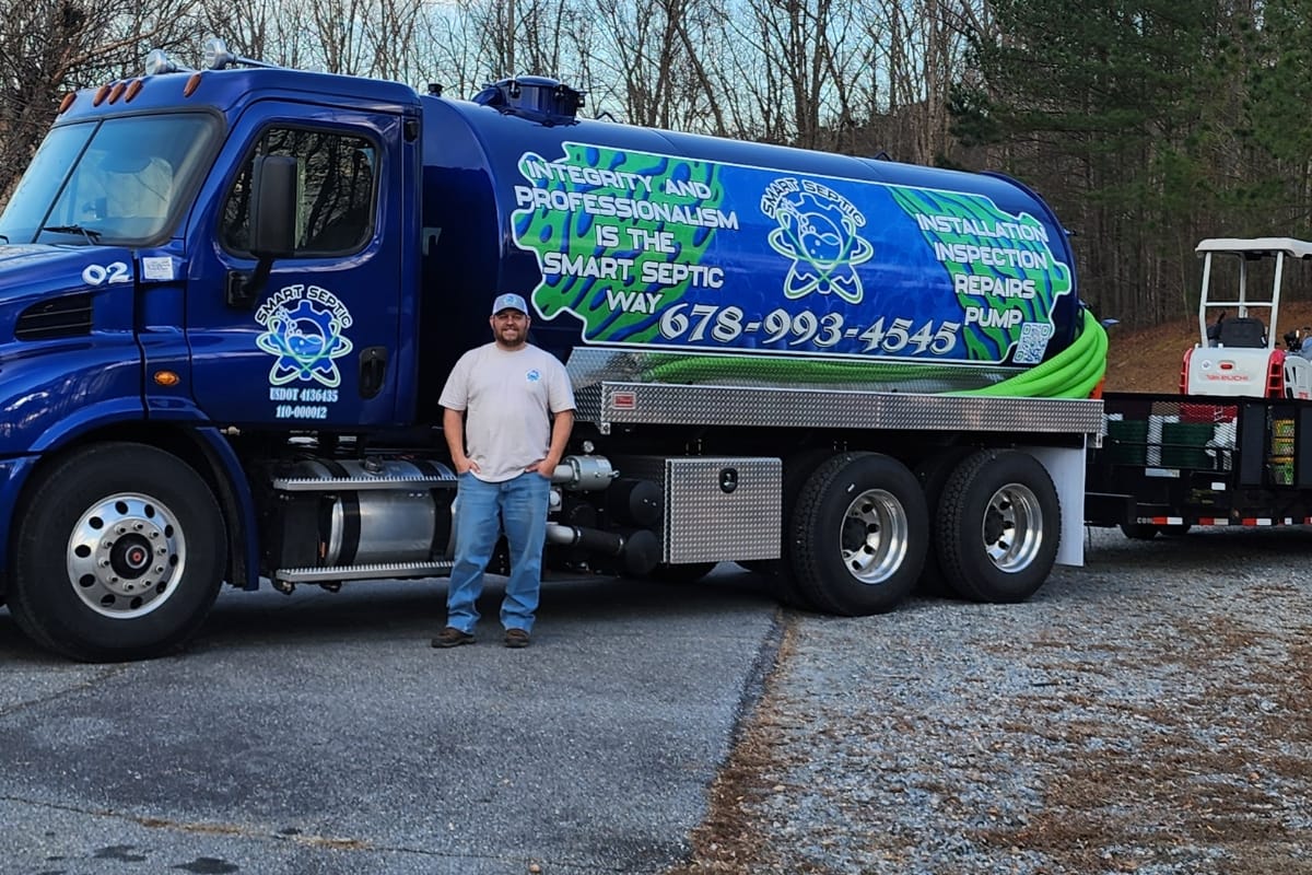 A man stands in front of a blue septic service truck, ready to bust common Septic System Myths, with company branding and contact information displayed on the side.