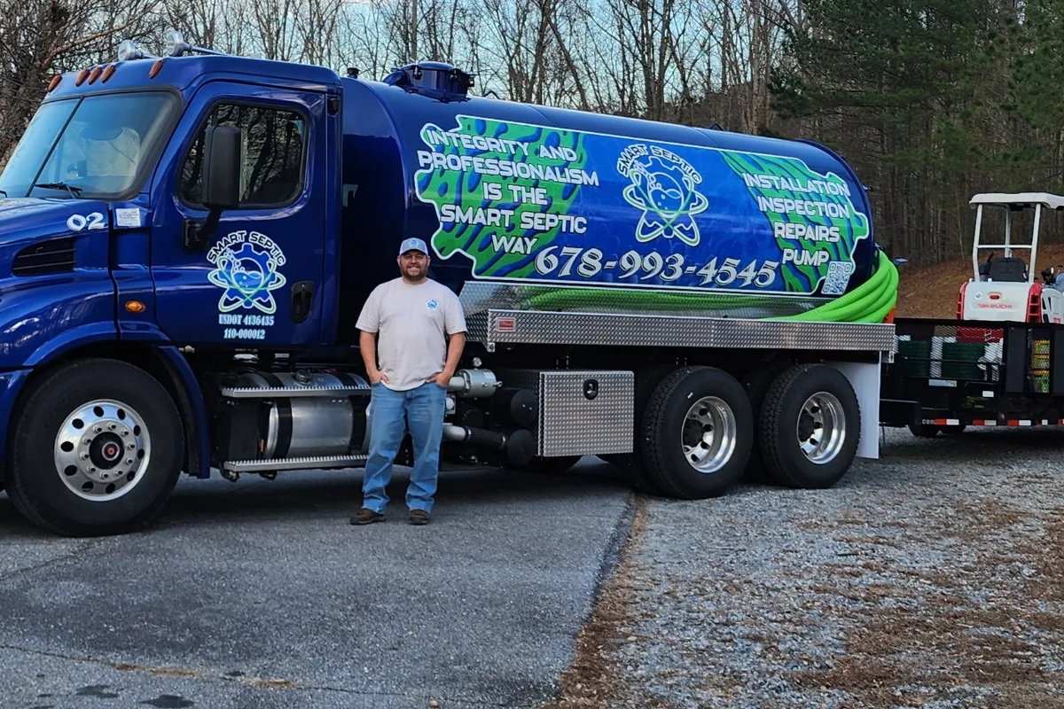 A man stands in front of a blue septic service truck, ready to bust common Septic System Myths, with company branding and contact information displayed on the side.