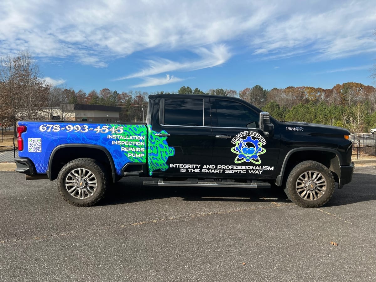 Fall Septic Maintenance in Acworth, GA: Preparing Your System 12 A black pickup truck with colorful business graphics advertising septic maintenance services, parked on asphalt with trees and a blue sky in the background.