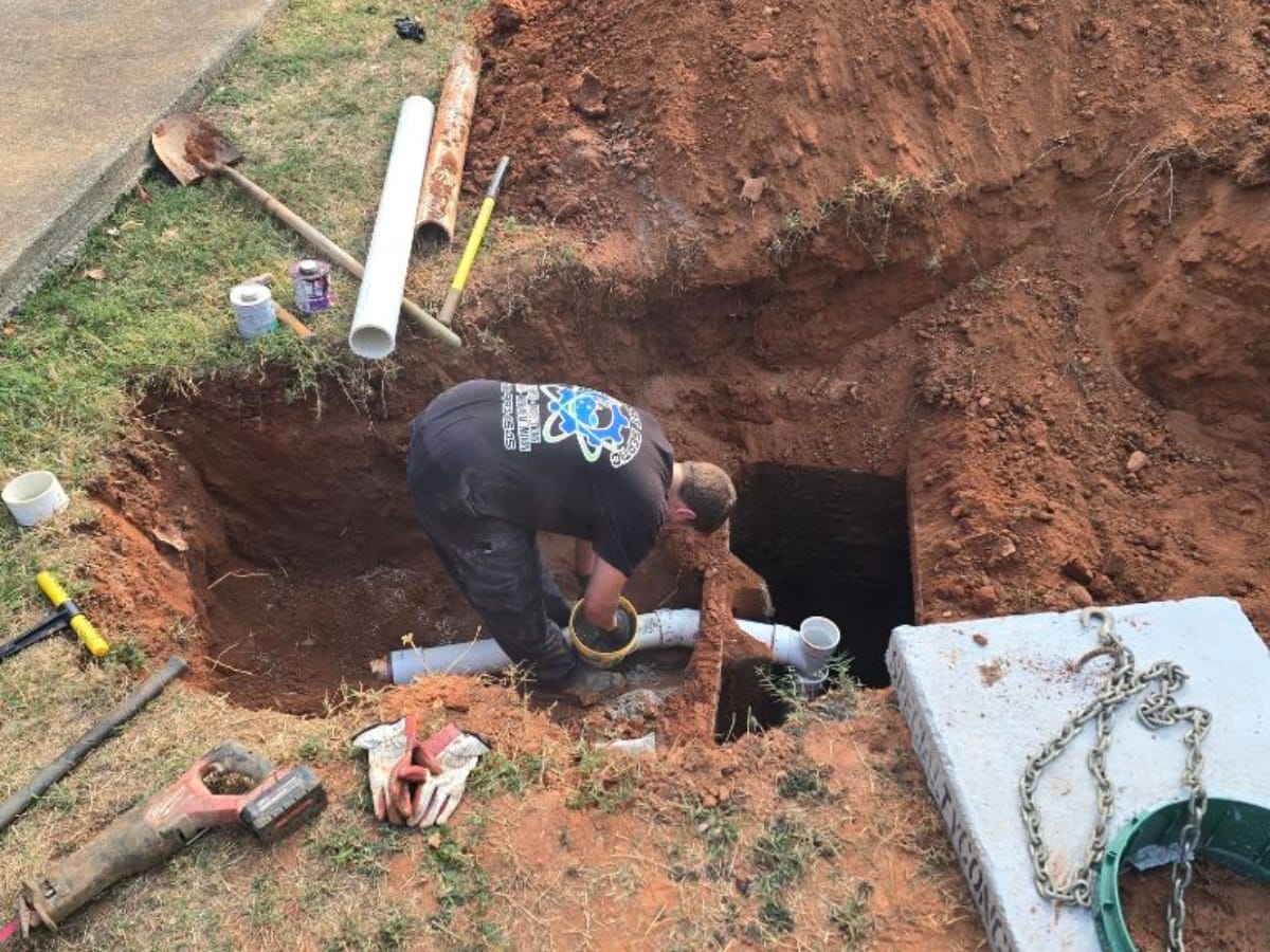 Septic System Components in Marietta, GA: Understanding the Basics 8 A worker installs PVC pipes in a trench dug in the ground, surrounded by tools and dirt—possibly as part of septic system components for plumbing or drainage work.