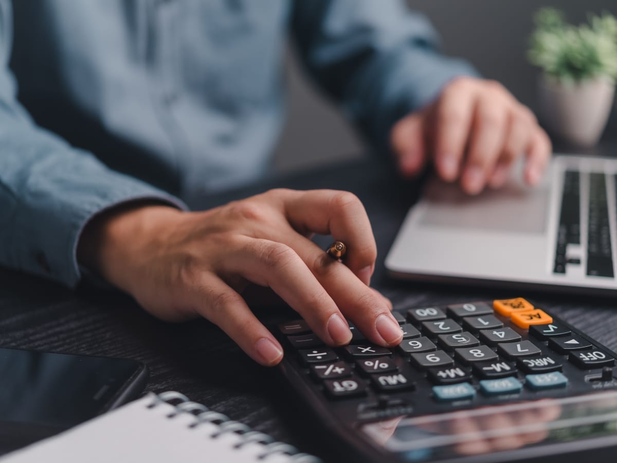 Septic System Components in Marietta, GA: Understanding the Basics 14 A person uses a calculator with one hand while typing on a laptop with the other; notes about septic system components are open in a notebook, alongside a pen and smartphone on the desk.