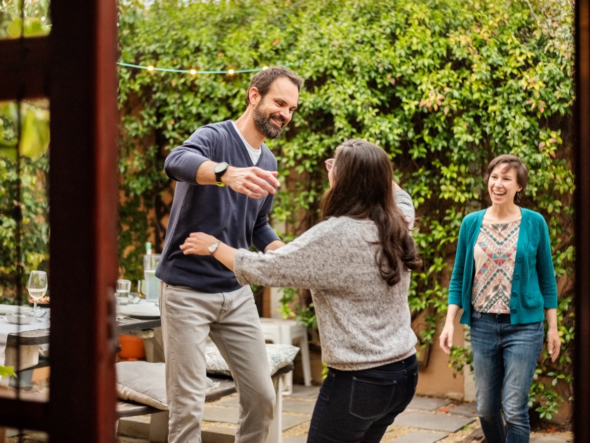 Holiday Septic Tips in Acworth, GA: Preparing for Guests 5 Three adults are smiling and dancing together in a backyard garden, with a table and chairs visible in the background—celebrating while sharing Holiday Septic Tips to keep gatherings stress-free.
