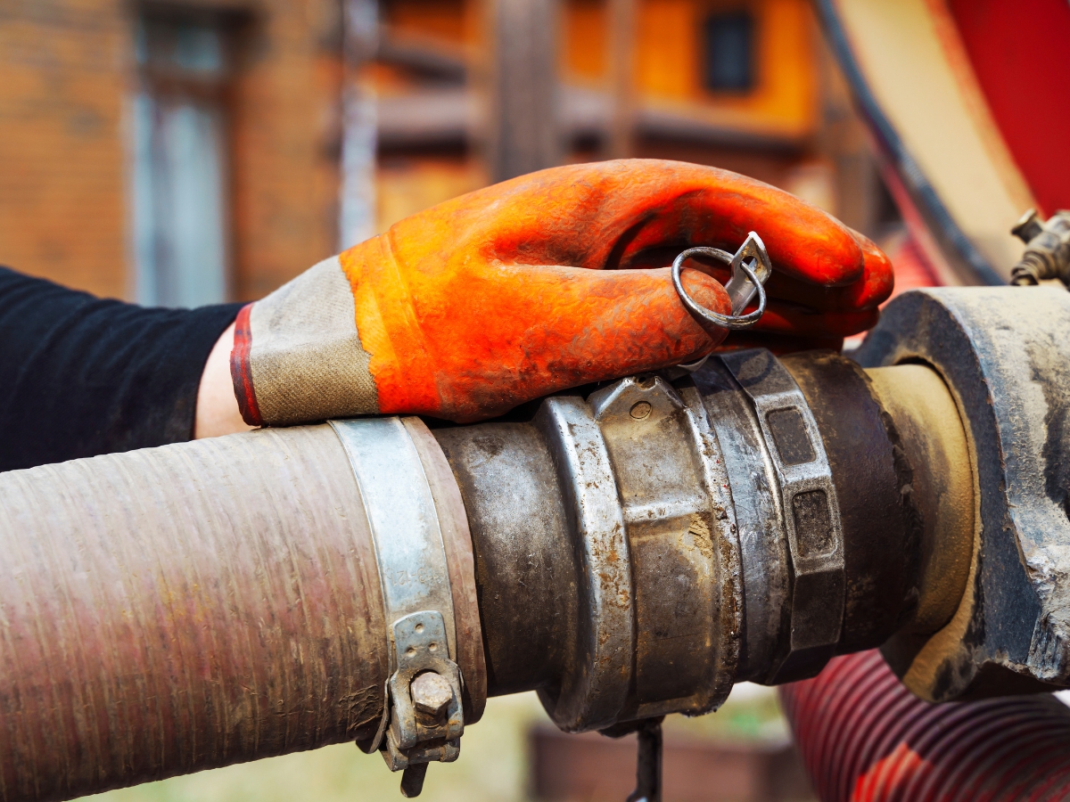 A person wearing an orange work glove secures a large industrial hose connection with a metal latch, following a year-end septic checklist in Kennesaw.