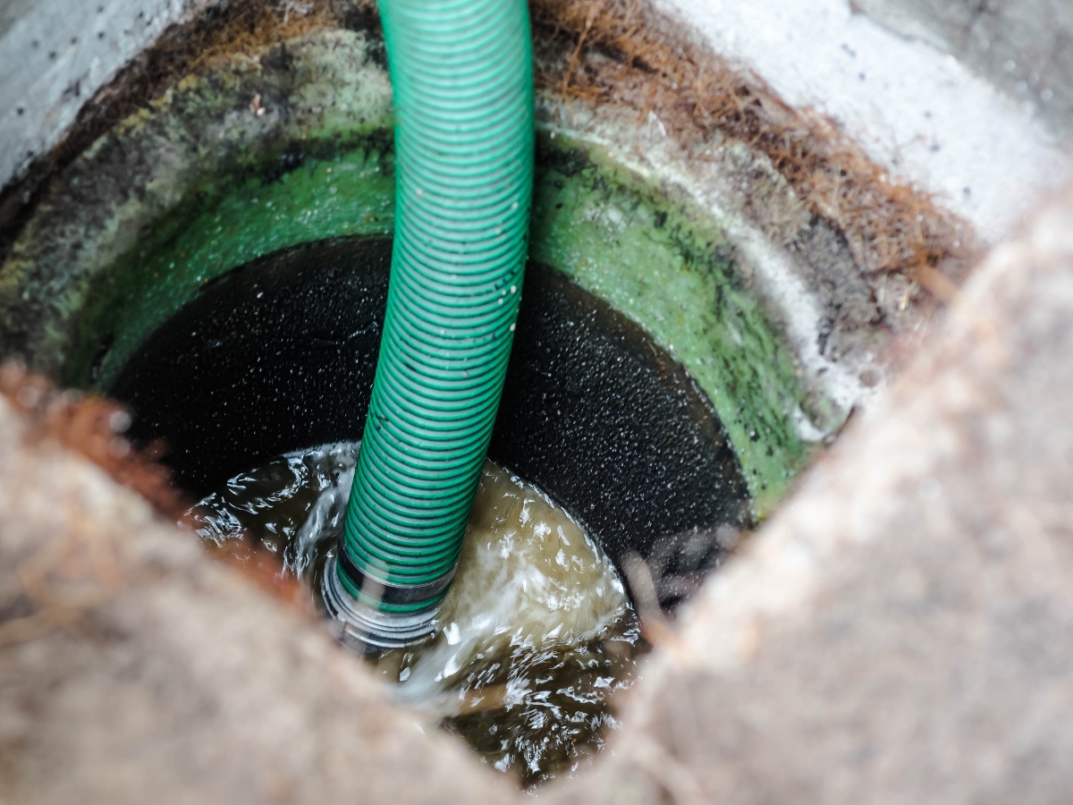 Septic System Emergency Preparedness: What to Do 3 A green hose is inserted into a round, concrete opening, suctioning dirty water from what appears to be a septic or drainage system—an important step in emergency prep.
