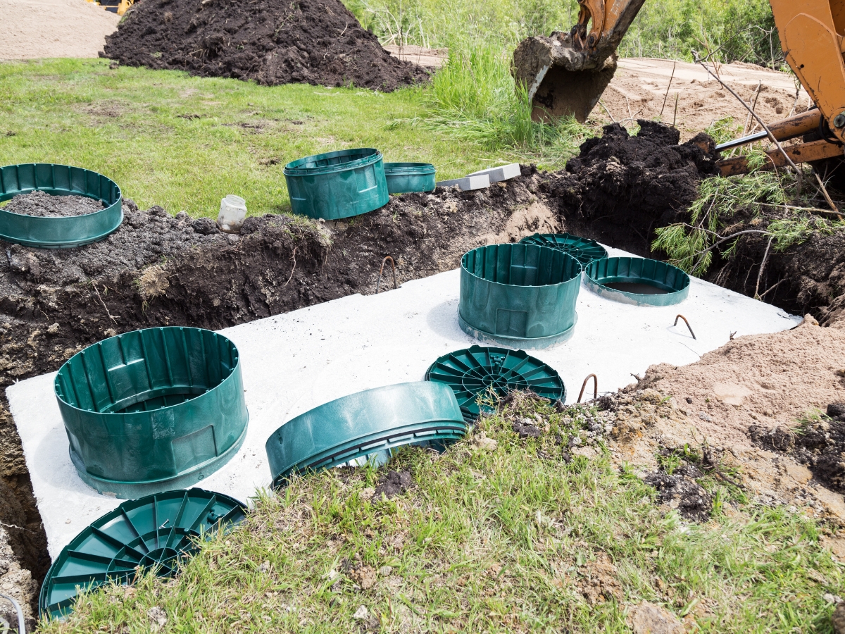 Concrete septic tank installation site featuring green plastic risers and lids, surrounded by dirt piles and construction equipment, showcases how new technologies enhance modern septic system efficiency.