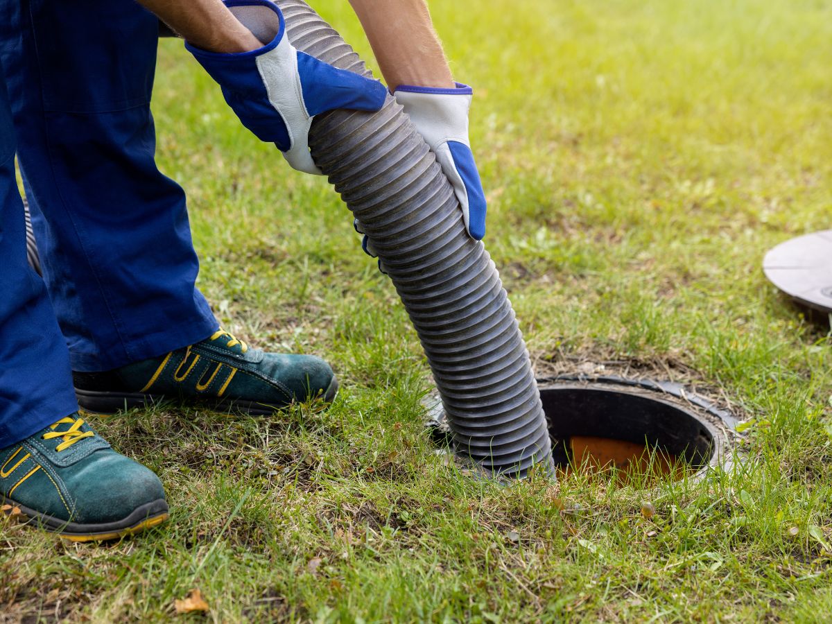 A person wearing gloves holds a large hose, inserting it into an open ground-level sewer or septic tank during an RV pumping process.