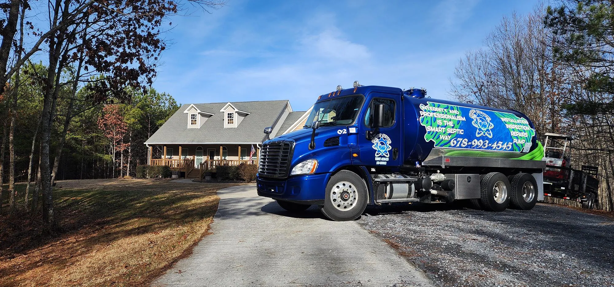 Blue truck parked on gravel driveway beside a large house surrounded by trees.